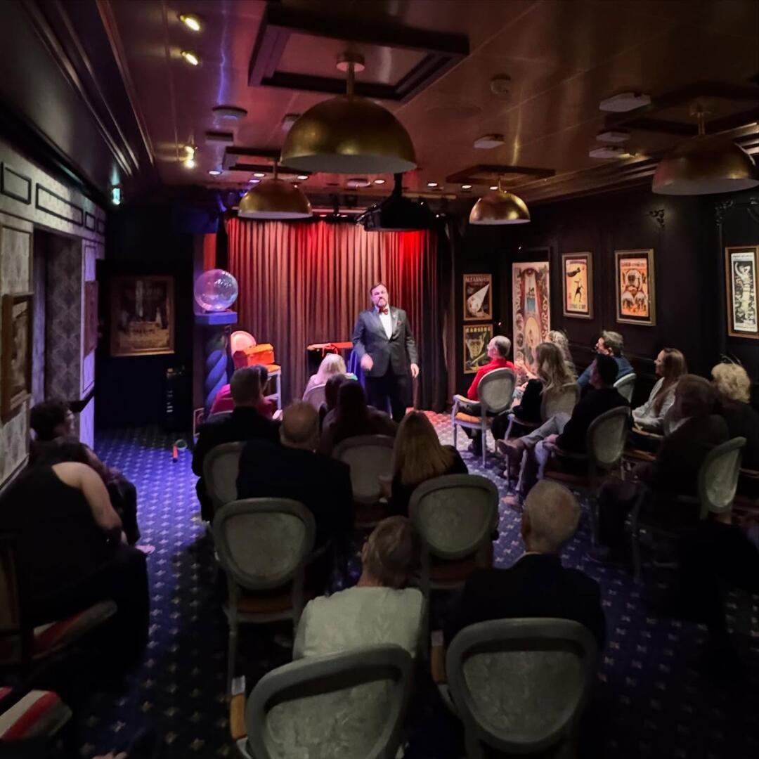 In an elegant venue, Matt Donnelly delivers a masterful performance to a captivated audience in a dimly lit, vintage-style setting.